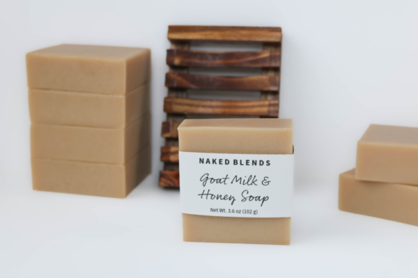 Goat Milk and Honey Soap bar in front of a wooden soap dish and stacks of other goat milk soaps