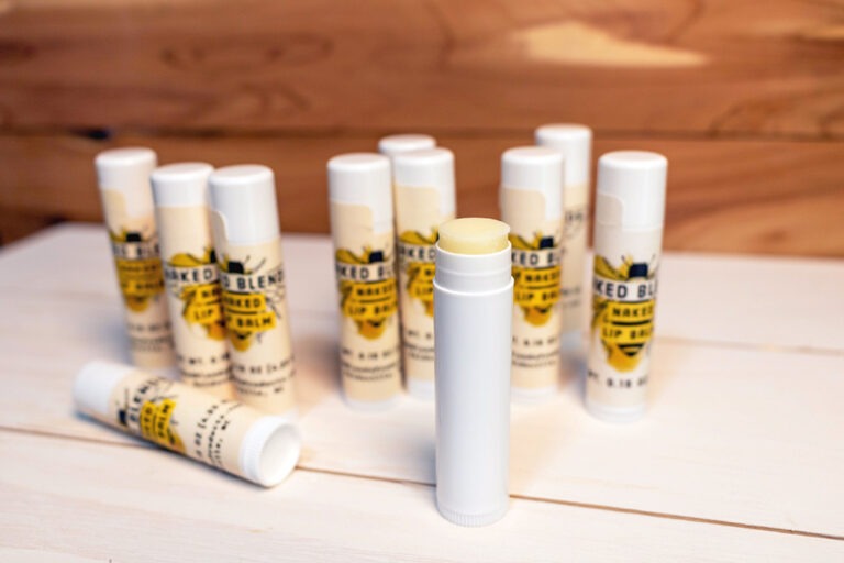 Naked Lip Balms with some standing upright, one on its side, and one unlabeled with the cap off exposing the lip balm