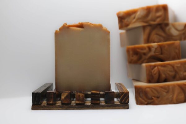 Amber Cocoa Butter Soap bar on a wooden soap dish with a stack of soaps in the background, handcrafted