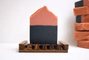Black Cherry Lemonade Soap bar on a wooden soap dish with layers of pink kaolin clay and charcoal