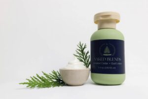 Smoked Cedar and Oud Lotion with cedar sprig and bowl of lotion on a white background.