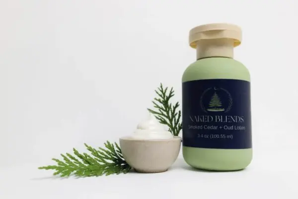 Smoked Cedar and Oud Lotion bottle with cedar sprig and bowl of creamy lotion