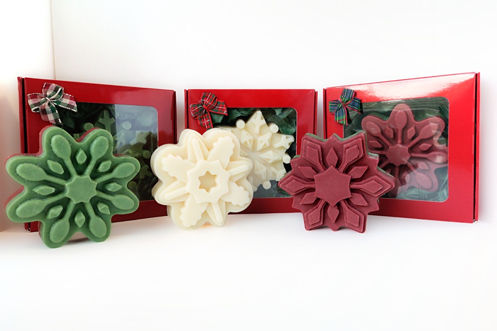 Snowflake Soap Gift in all three colors, green top, white, and red top snowflake soaps standing in front of three red gift boxes with plaid bows, each box showing a snowflake soap inside.