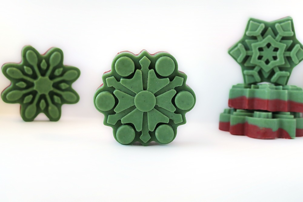 Green-topped snowflake soaps standing and stacked, showing the red layer of the red and green layered bars along the sides
