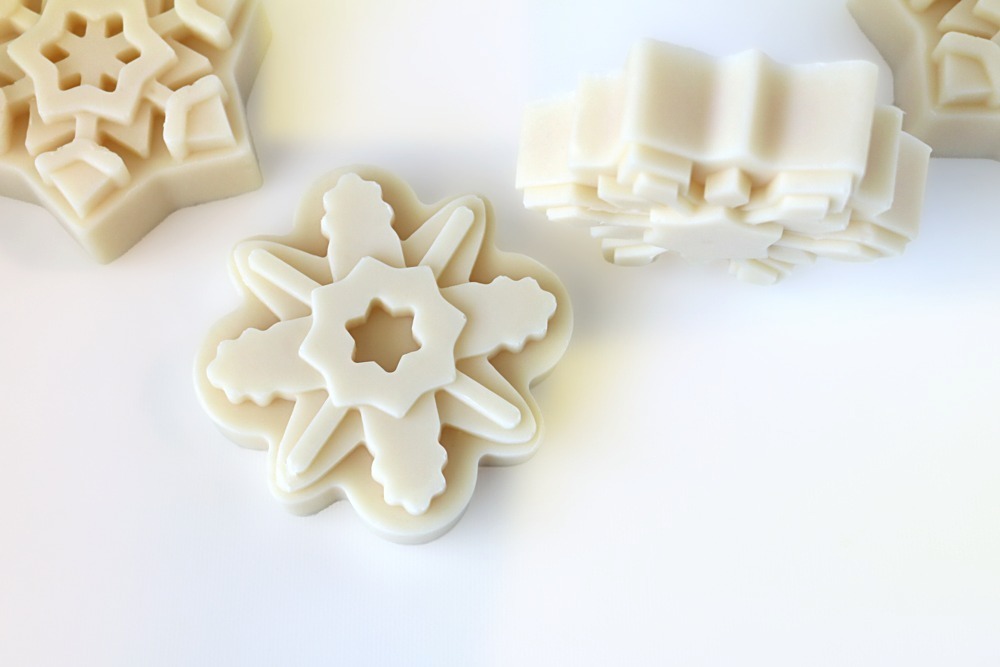 White snowflake soaps in different designs on a white background, one turned on its side showing the thickness of the bar